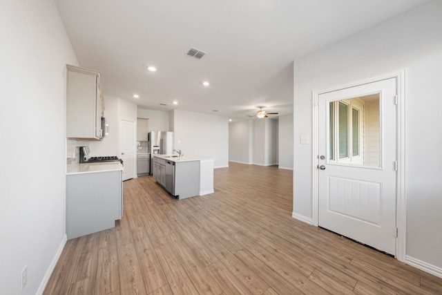 kitchen with tasteful backsplash, ceiling fan, light wood-type flooring, a kitchen island with sink, and stainless steel fridge