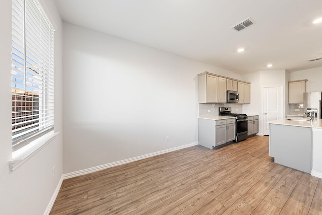 kitchen featuring appliances with stainless steel finishes, sink, backsplash, gray cabinets, and light wood-type flooring