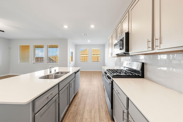 kitchen with tasteful backsplash, gray cabinets, sink, light hardwood / wood-style flooring, and appliances with stainless steel finishes