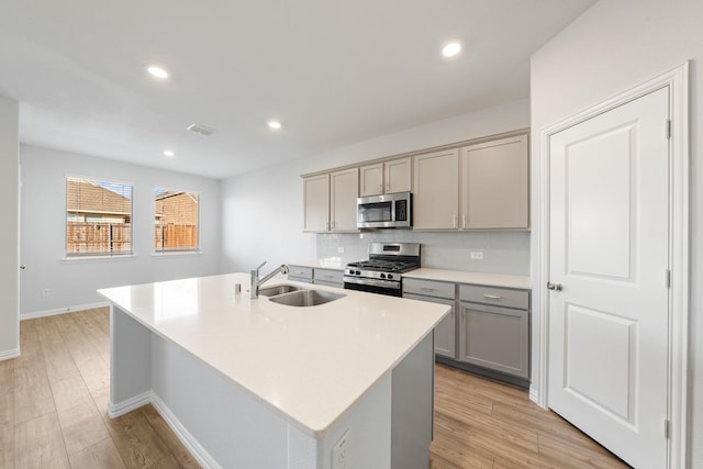 kitchen featuring stainless steel appliances, sink, a kitchen island with sink, and gray cabinets