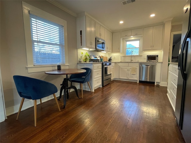 kitchen featuring white cabinets, appliances with stainless steel finishes, dark wood-type flooring, decorative backsplash, and crown molding