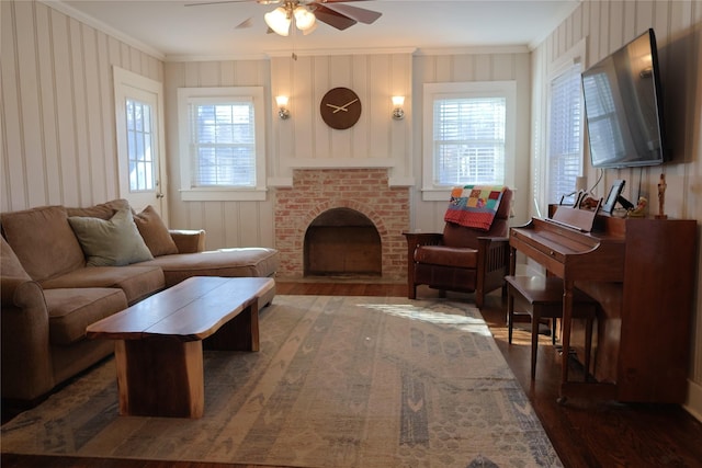 living room with ceiling fan, a brick fireplace, dark hardwood / wood-style floors, and crown molding