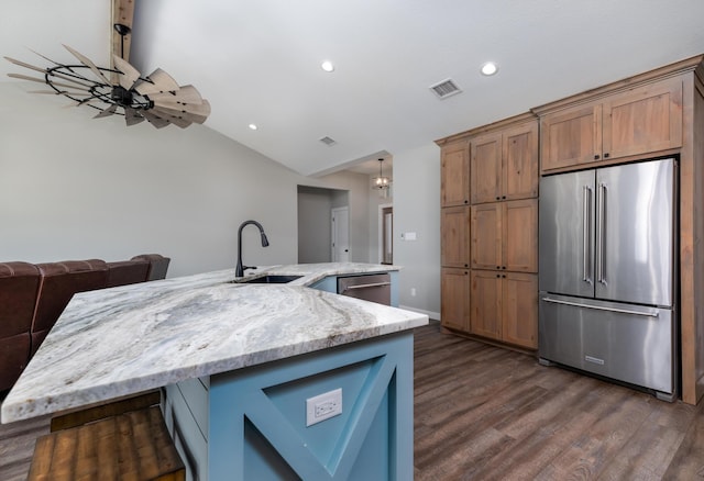 kitchen featuring sink, appliances with stainless steel finishes, dark hardwood / wood-style floors, light stone countertops, and a large island with sink