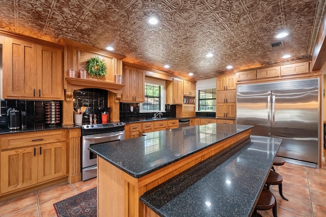 kitchen with a kitchen island, sink, a kitchen breakfast bar, stainless steel appliances, and dark stone counters