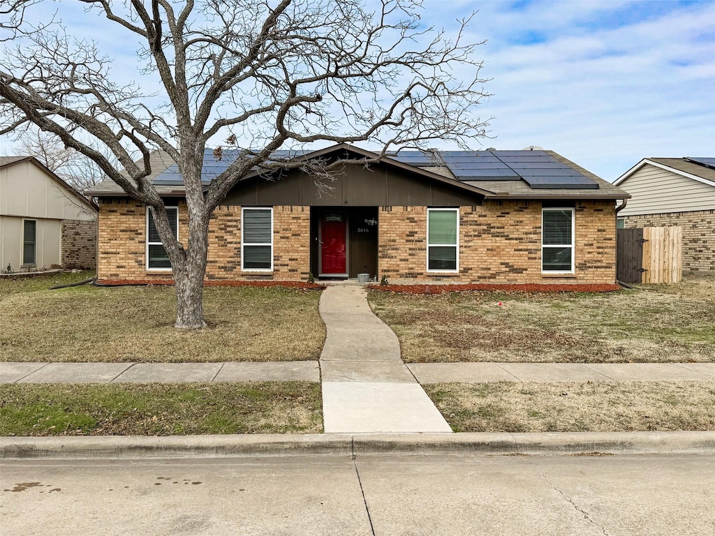 ranch-style home featuring a front lawn and solar panels