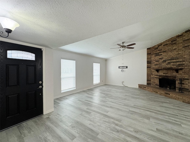 foyer entrance with ceiling fan, light wood-type flooring, a brick fireplace, and a textured ceiling