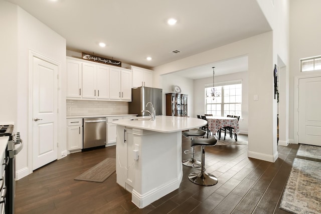 kitchen featuring decorative light fixtures, a kitchen bar, a kitchen island with sink, stainless steel appliances, and white cabinets