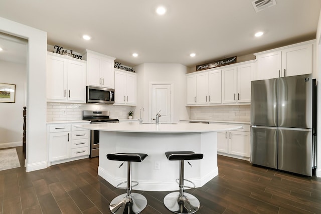 kitchen featuring white cabinets, decorative backsplash, stainless steel appliances, and a center island with sink