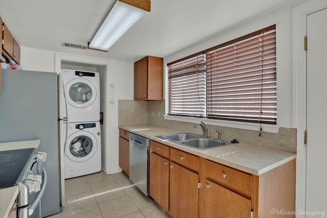 kitchen featuring stacked washer and dryer, light tile patterned floors, appliances with stainless steel finishes, backsplash, and sink