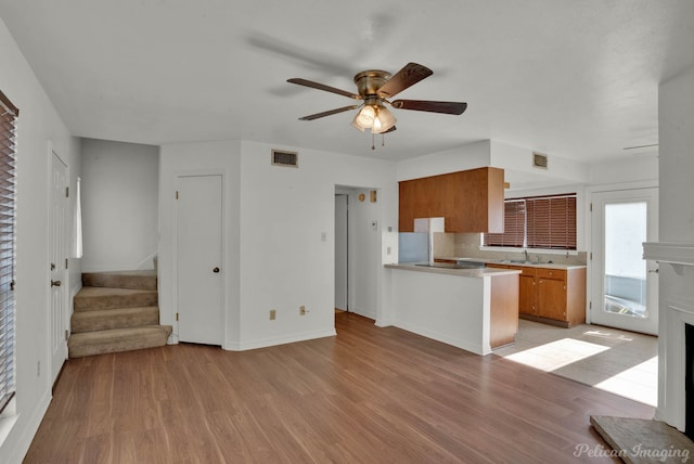 kitchen with light hardwood / wood-style floors, kitchen peninsula, a brick fireplace, ceiling fan, and backsplash