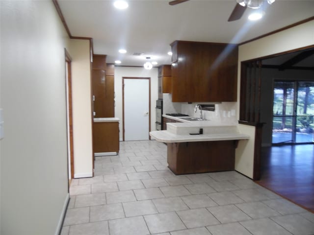 kitchen with a kitchen bar, kitchen peninsula, ceiling fan, ornamental molding, and sink