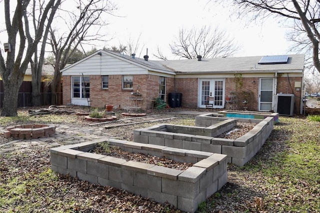 rear view of property with solar panels, an outdoor fire pit, french doors, and central air condition unit