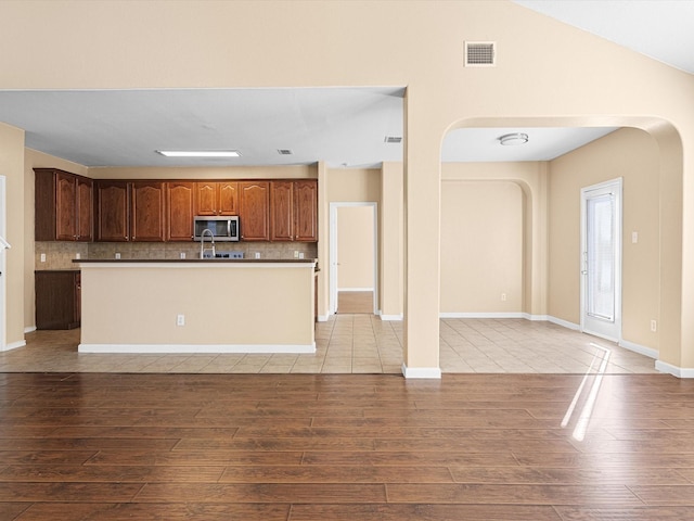 kitchen featuring a kitchen island with sink, backsplash, vaulted ceiling, and light hardwood / wood-style floors