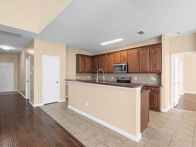 kitchen featuring light tile patterned flooring, an island with sink, stainless steel appliances, and tasteful backsplash