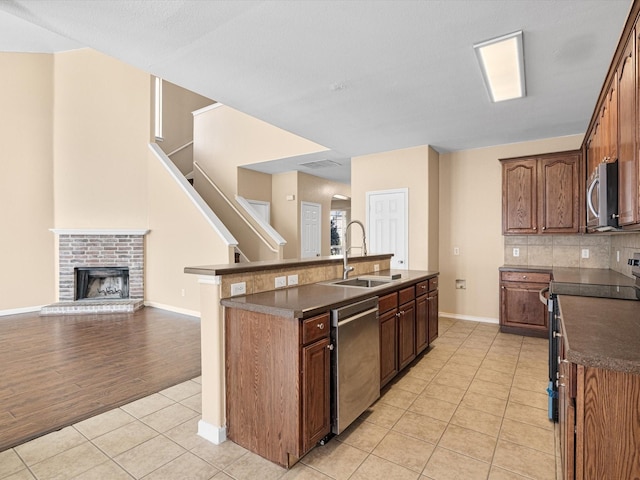 kitchen featuring a fireplace, a center island with sink, sink, light tile patterned flooring, and stainless steel appliances