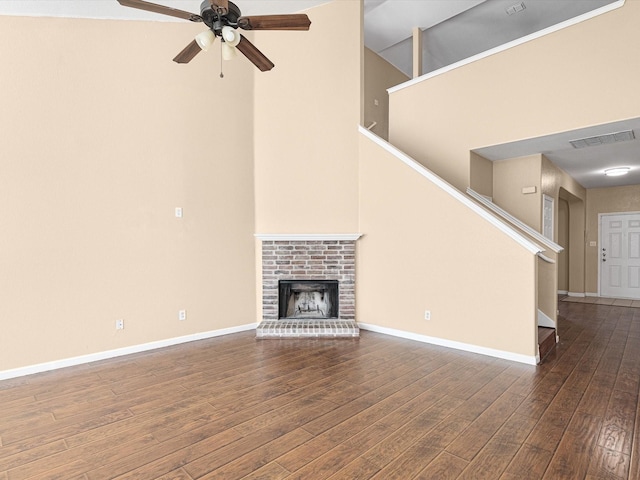 unfurnished living room featuring a high ceiling, a brick fireplace, dark hardwood / wood-style floors, and ceiling fan