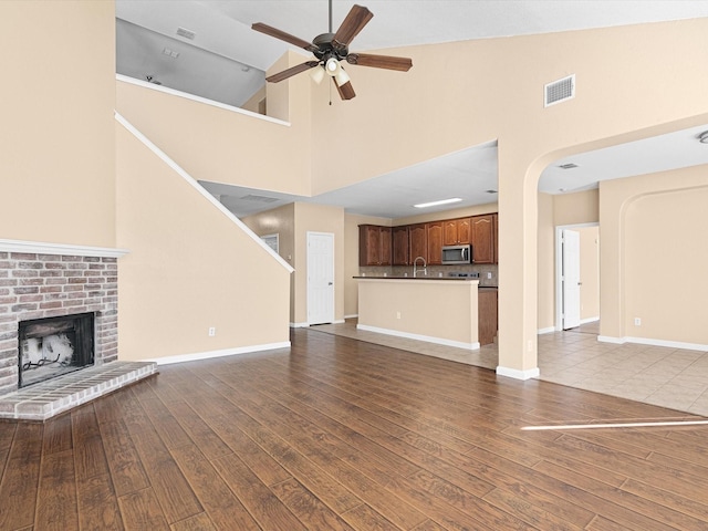 unfurnished living room with hardwood / wood-style flooring, a brick fireplace, ceiling fan, high vaulted ceiling, and sink