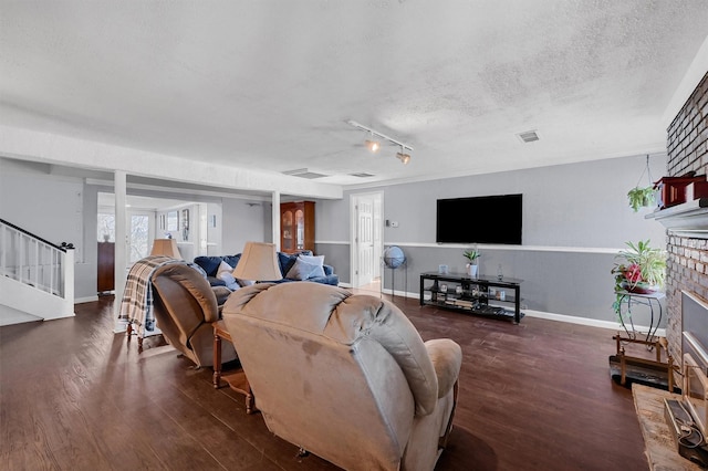 living room with a brick fireplace, dark wood-type flooring, and a textured ceiling