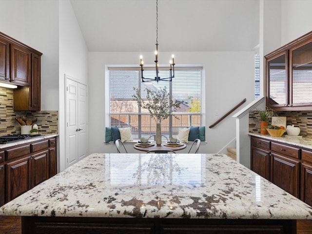 kitchen featuring decorative backsplash, lofted ceiling, a chandelier, dark brown cabinetry, and a center island