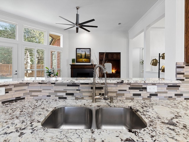 kitchen with ceiling fan, sink, crown molding, and light stone countertops