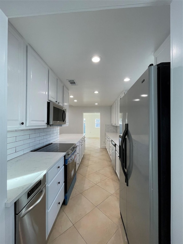 kitchen featuring light tile patterned floors, stainless steel appliances, tasteful backsplash, light stone countertops, and white cabinets