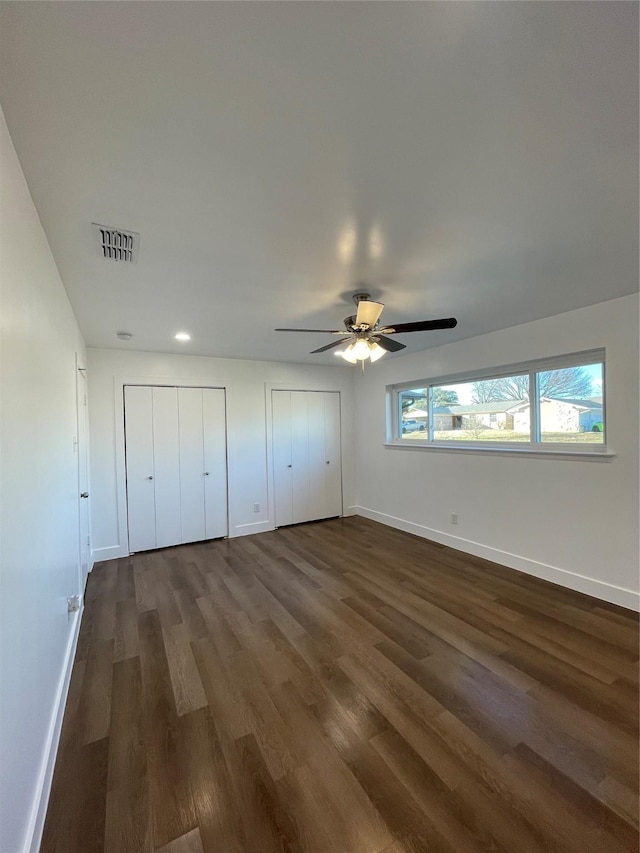 unfurnished bedroom with ceiling fan, dark hardwood / wood-style flooring, and multiple closets