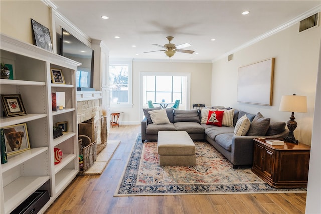 living room with ceiling fan, ornamental molding, a fireplace, and light hardwood / wood-style flooring