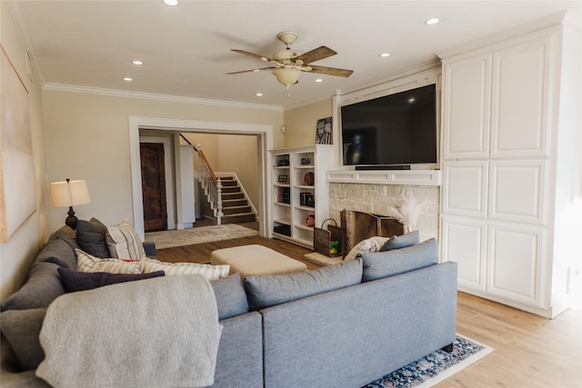 living room with ceiling fan, a stone fireplace, ornamental molding, and light hardwood / wood-style floors