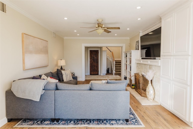 living room with ceiling fan, ornamental molding, light hardwood / wood-style flooring, and a stone fireplace