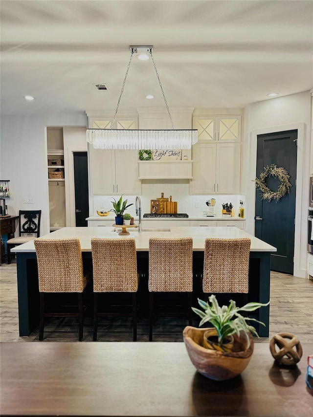 bar featuring visible vents, stainless steel oven, decorative backsplash, light wood-style floors, and a sink