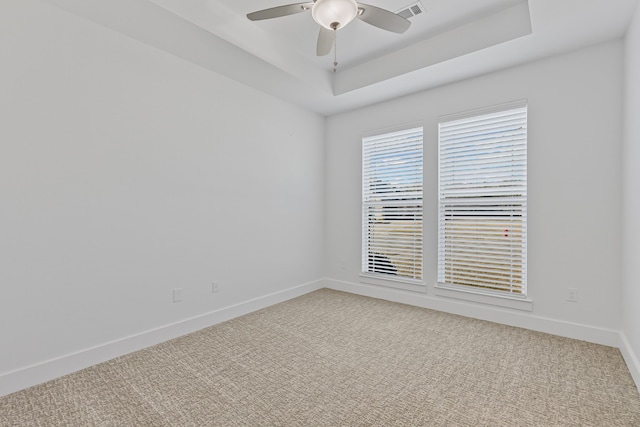 unfurnished room with visible vents, light carpet, a tray ceiling, baseboards, and ceiling fan