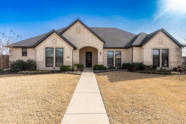 french country home with brick siding, a front yard, and a shingled roof