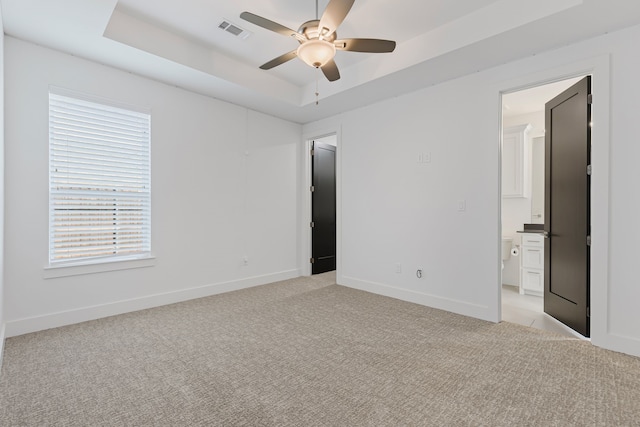 unfurnished bedroom featuring visible vents, baseboards, light colored carpet, ensuite bathroom, and a raised ceiling