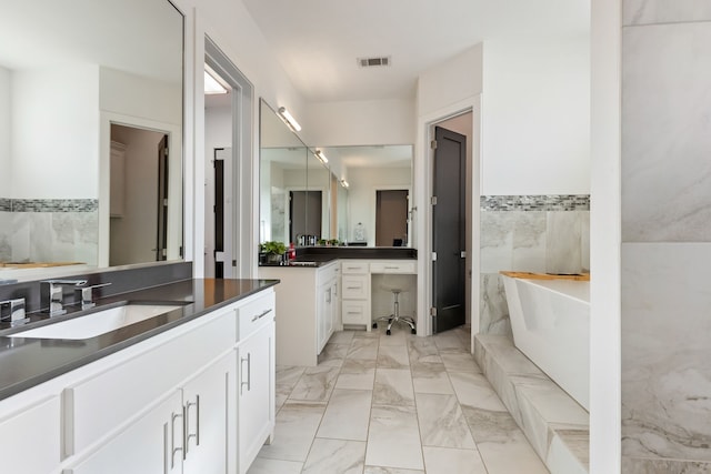 full bath with marble finish floor, two vanities, a sink, tile walls, and a freestanding bath