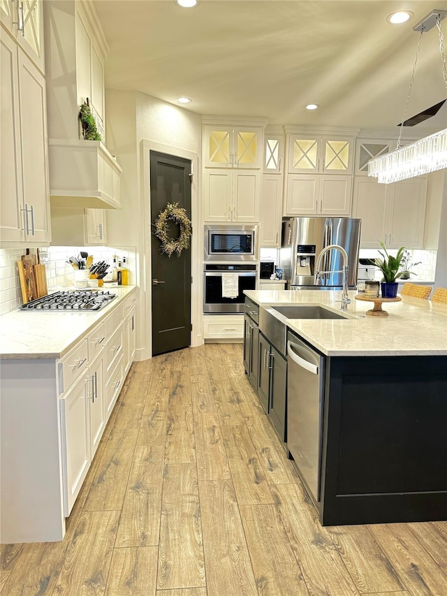 kitchen featuring decorative light fixtures, backsplash, light hardwood / wood-style floors, white cabinetry, and appliances with stainless steel finishes