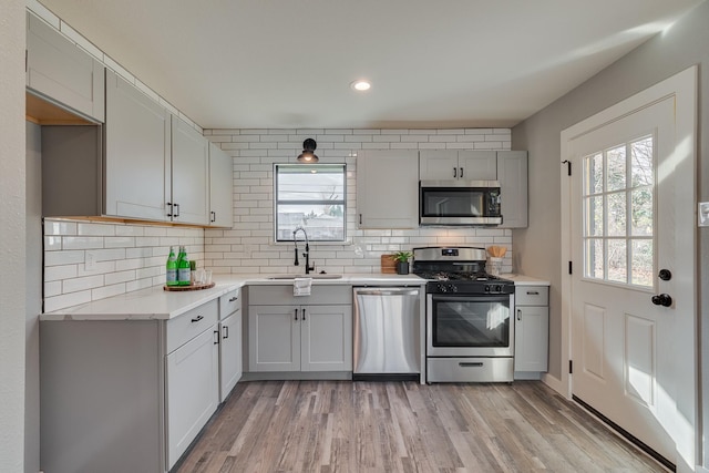 kitchen with stainless steel appliances, light hardwood / wood-style flooring, backsplash, and sink