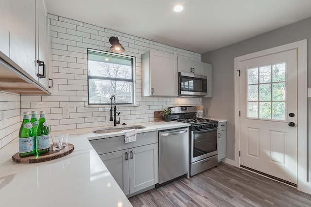 kitchen with wood-type flooring, sink, appliances with stainless steel finishes, white cabinets, and light stone counters