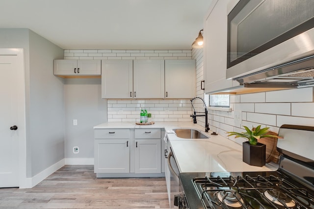 kitchen featuring pendant lighting, sink, white cabinetry, light wood-type flooring, and appliances with stainless steel finishes