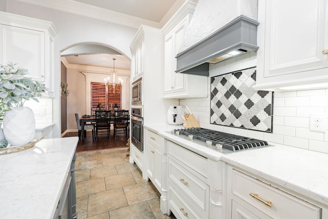 kitchen featuring ornamental molding, custom range hood, stainless steel appliances, light stone countertops, and white cabinets