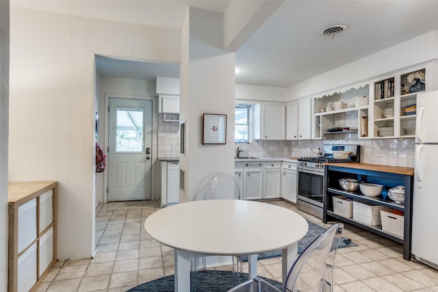 kitchen with tasteful backsplash, stainless steel range with gas stovetop, white cabinetry, butcher block counters, and white refrigerator