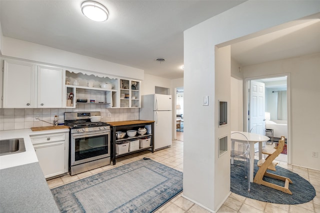 kitchen with white fridge, white cabinetry, stainless steel range with gas cooktop, decorative backsplash, and sink