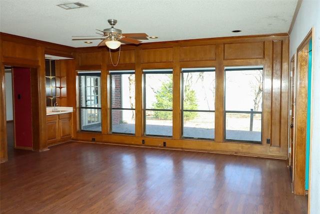 interior space with ceiling fan, dark wood-type flooring, crown molding, and wooden walls