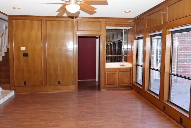 interior space with dark hardwood / wood-style flooring, sink, wood walls, ornamental molding, and ceiling fan