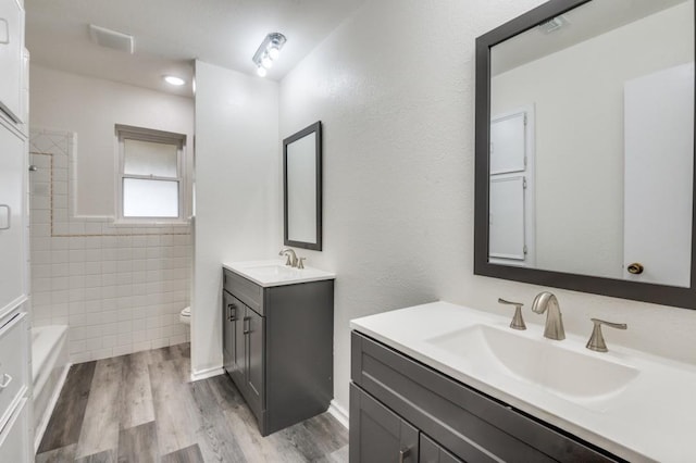 full bath featuring wood finished floors, two vanities, a sink, and toilet