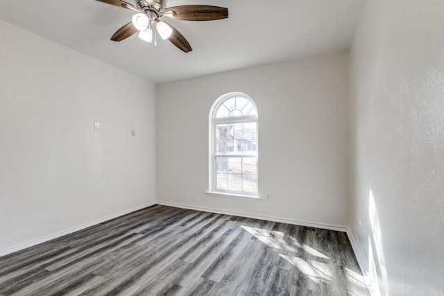 spare room featuring dark wood-type flooring, a ceiling fan, and baseboards