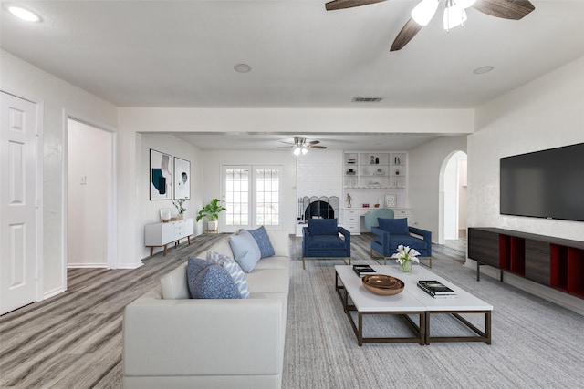 living room featuring baseboards, visible vents, arched walkways, ceiling fan, and wood finished floors