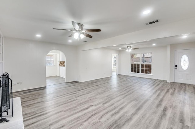 unfurnished living room with arched walkways, visible vents, and light wood-style flooring