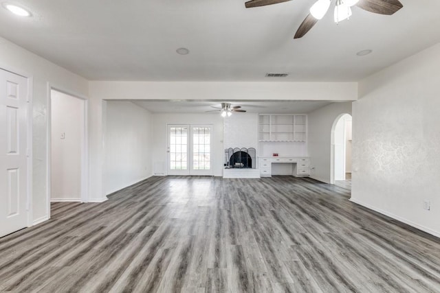 unfurnished living room featuring arched walkways, visible vents, a fireplace, and wood finished floors