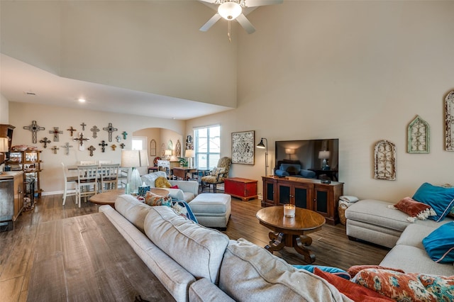 living room with dark wood-type flooring, a towering ceiling, and ceiling fan