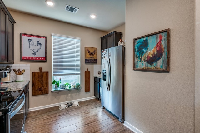 kitchen with stainless steel appliances, backsplash, wood-type flooring, light stone countertops, and dark brown cabinetry